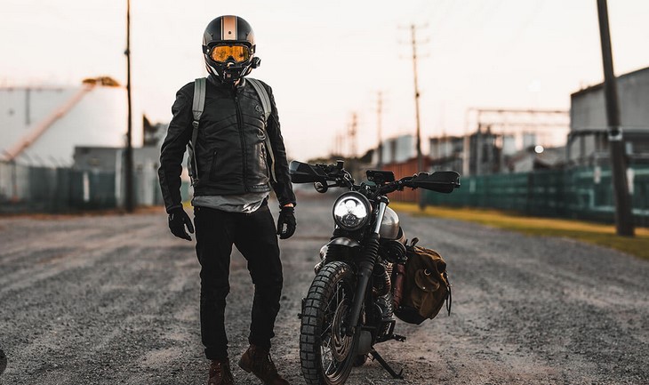 man wearing motorbike apparels and standing next to his bike 