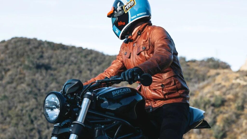 a man wearing a brown riding jacket sitting on his bike showing the concept of right motorbike jacket 